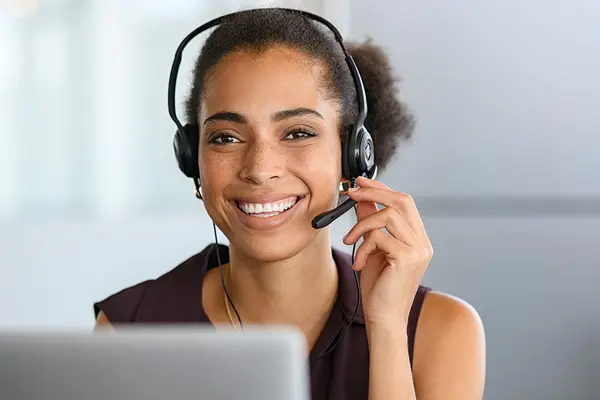 lächelnde Frau mit Headset vor Laptop
