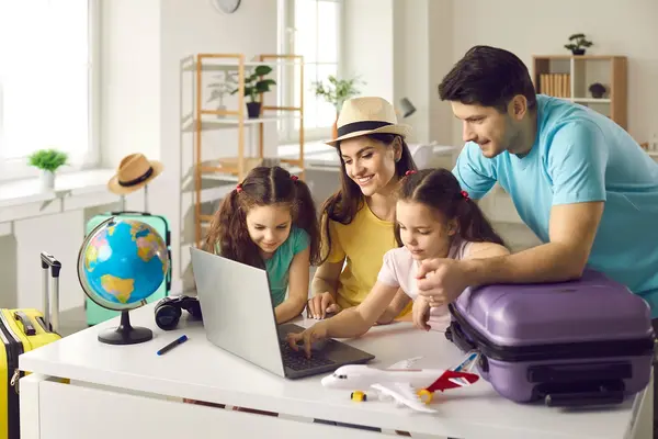 Eine Familie am Laptop. Daneben steht ein Reisekoffer.