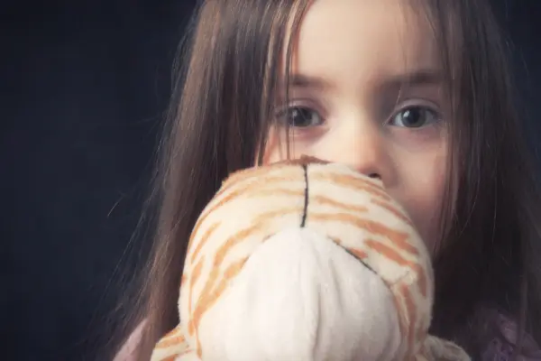 Ein verängstigtes Kind hält ein Kuscheltier vor das Gesicht.