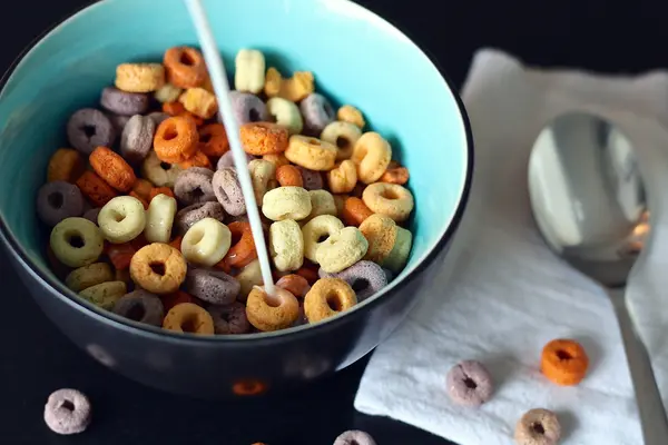 Schüssel mit bunten Frühstücksflocken, in die Milch eingegossen wird.