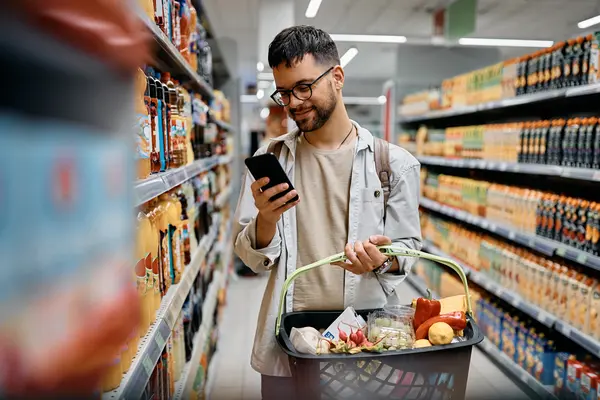 Mann kauft im Supermarkt ein unf schaut auf sein Smartphone