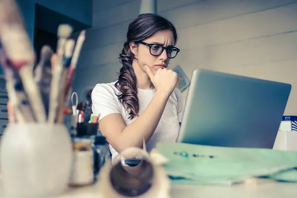 Eine Frau sitzt mit kritischem Blick am Schreibtisch vor ihrem Laptop
