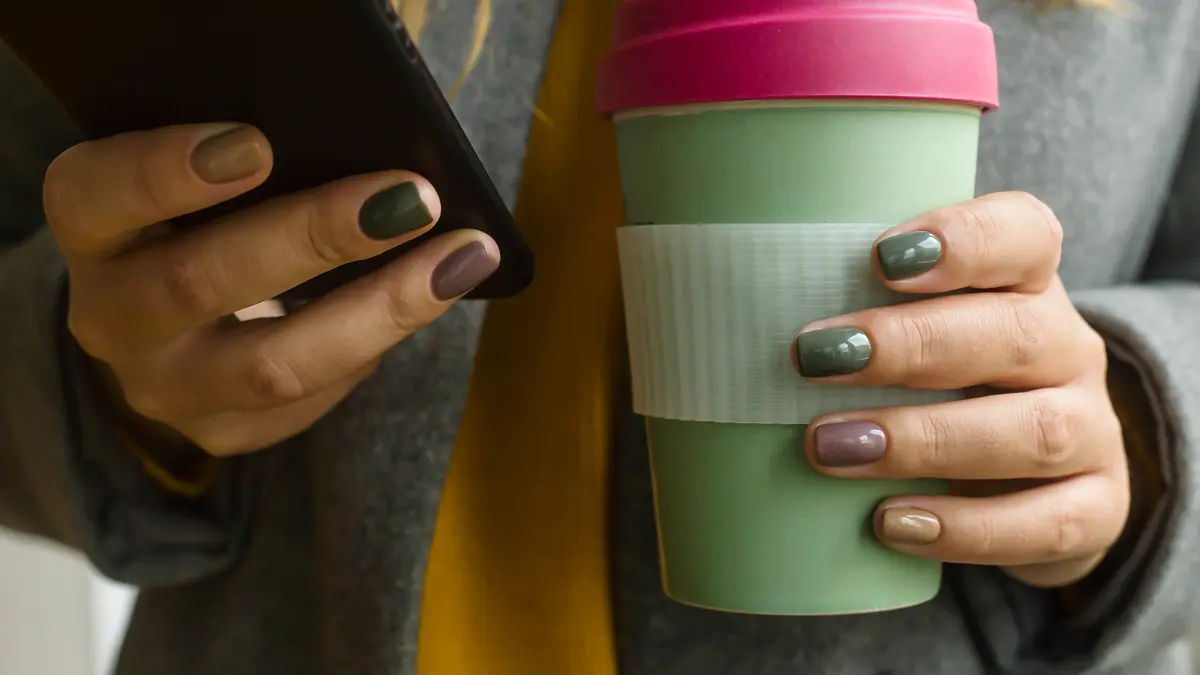 Junge Frau hält wiederverwertbaren Kaffeebecher in einer Hand