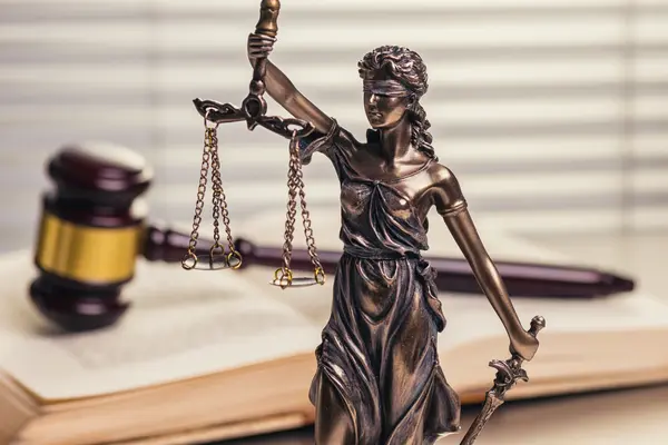 Justitia steht vor einem Buch und einem Hammer