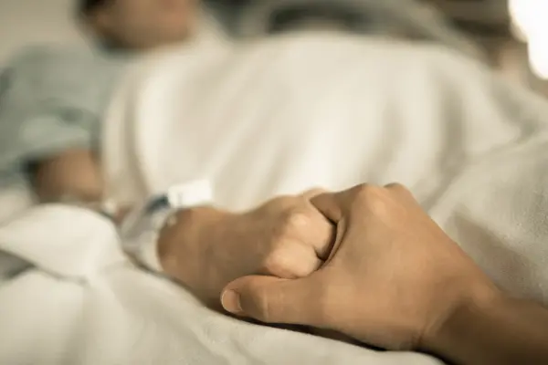 eine Hand hält die Hand einer in einem Krankenbett liegenden Person
