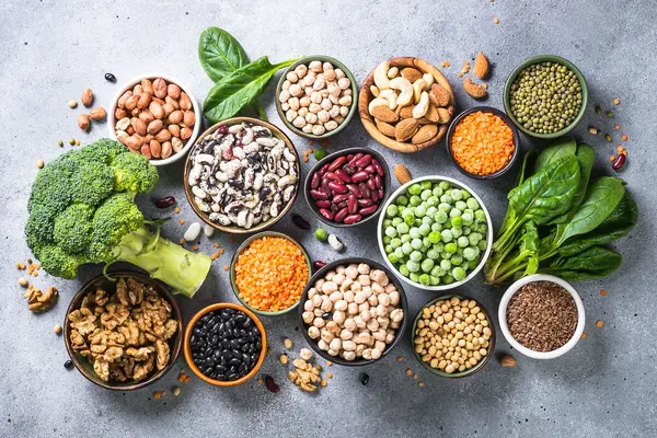 Verschiedene vegane eiweißreiche Lebensmittel, wie etwas Linsen, Bohnen oder Nüsse, liegen auf einem Tisch.