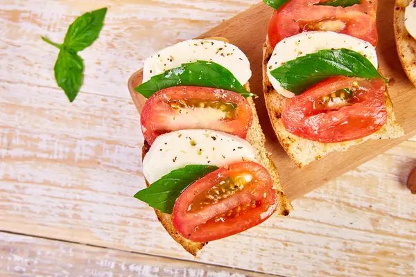 Bruschetta mit Tomate, Mozarella und Basilikum auf einem Brettchen