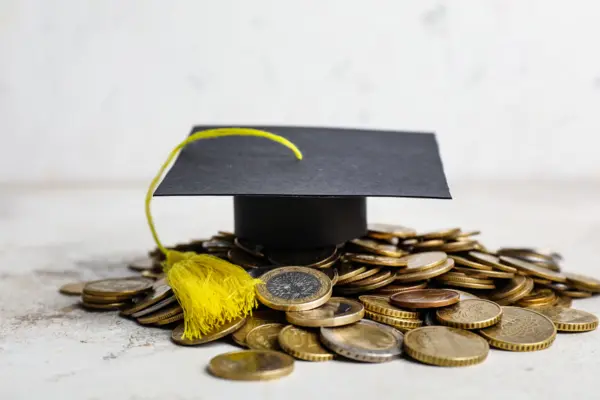 Absolventenhut liegt auf einem kleinen Haufen Euro und Cent Münzen
