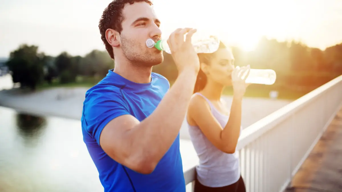 Sportler und Sportlerin trinken aus Flaschen, sie stehen auf einer Brücke im Abendlicht