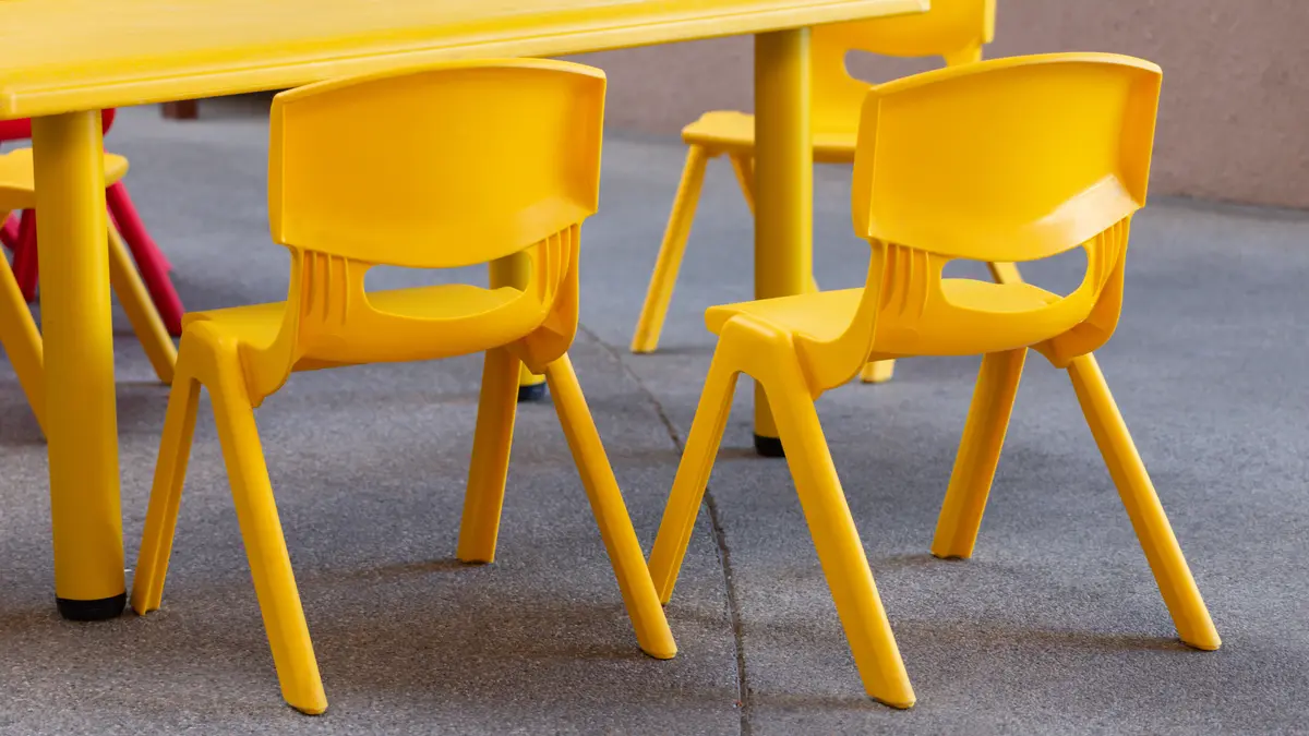 Ein gelber Kinderstuhl aus Plastik steht neben einem anderen gelben Plastikstuhl