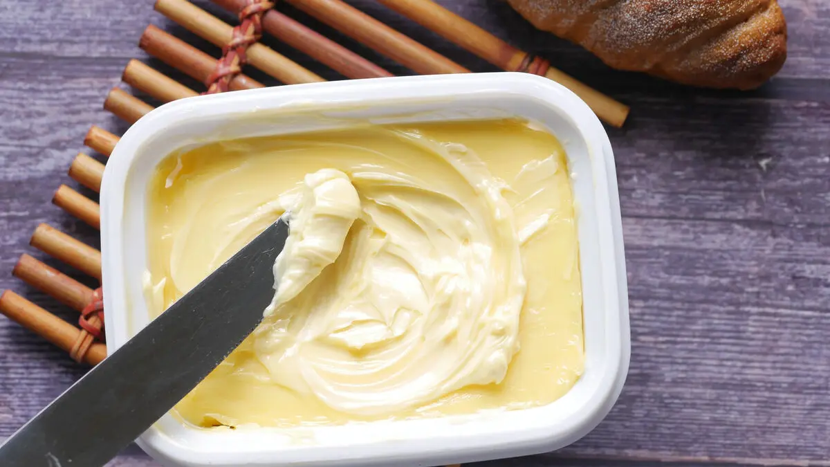 Eine offene Margarinepackung steht auf einem Tisch, ein Messer mit etwas Margarine liegt darauf.