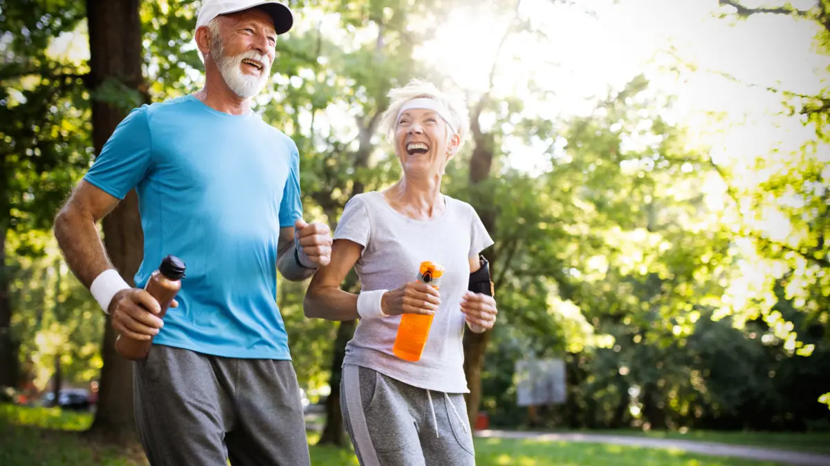 eine Seniorin und ein Senior bei einer leichten sportlichen Bewegung im Wald