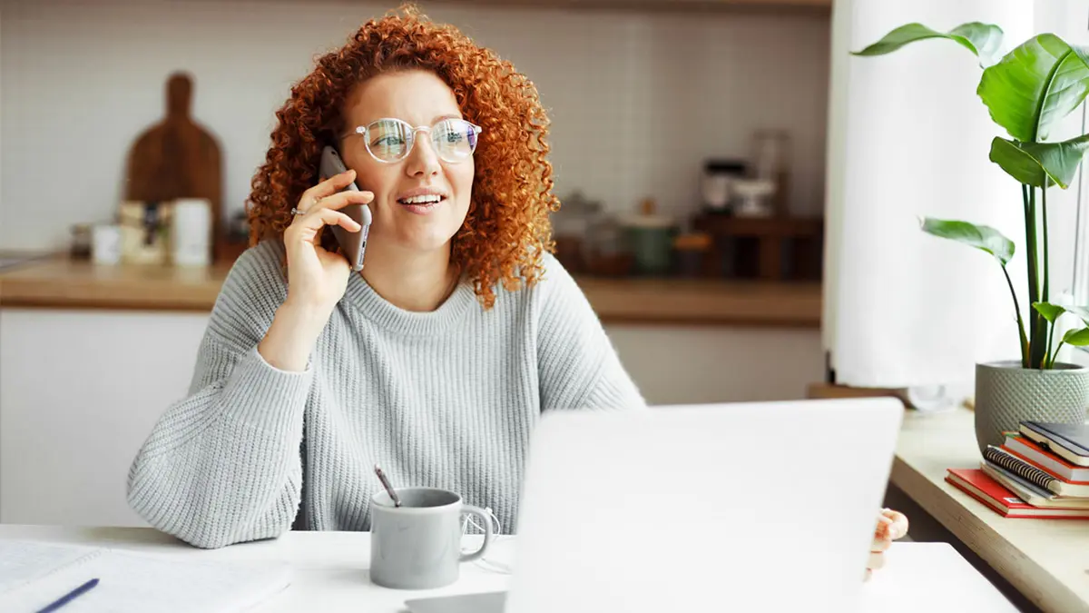 rothaarige Frau telefoniert am Wohnzimmertisch