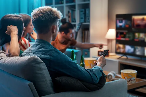 Junge Menschen sitzen auf dem Sofa und schauen Streaming-Angebote auf dem Smart-TV