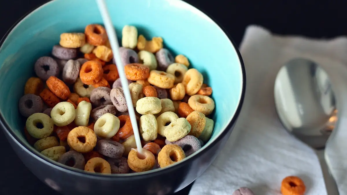 Schüssel mit bunten Frühstücksflocken, in die Milch eingegossen wird.