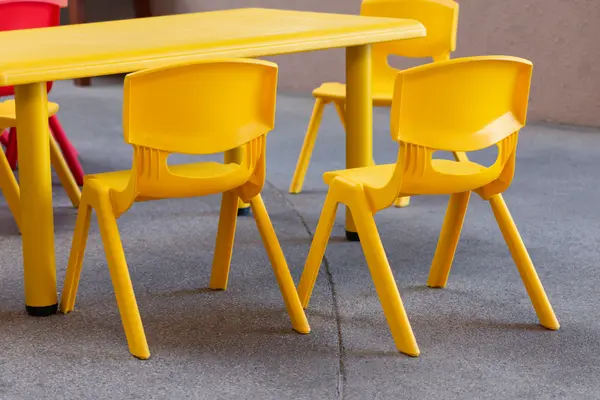 Ein gelber Kinderstuhl aus Plastik steht neben einem anderen gelben Plastikstuhl