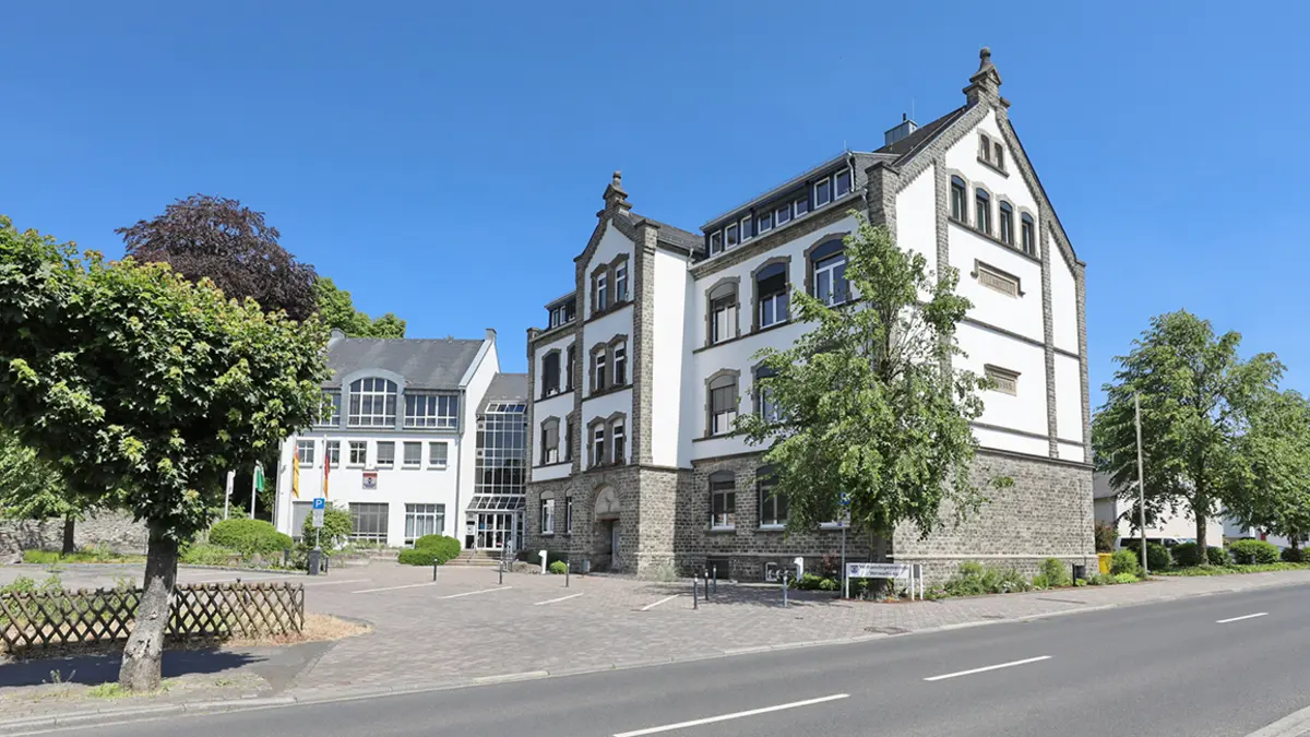 Ein Gebäude. Davor ein großer Platz mit einem Baum.