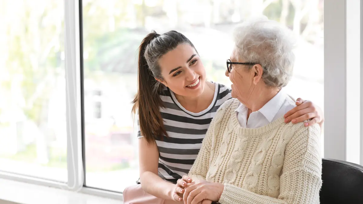 Eine pflegende Angehörige legt den Arm um eine Seniorin.