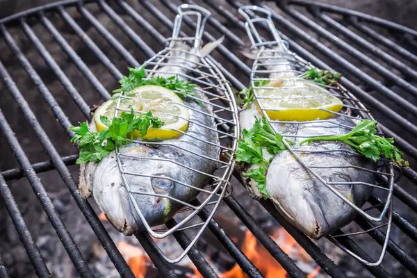 Fische in Grillzangen auf dem Grill