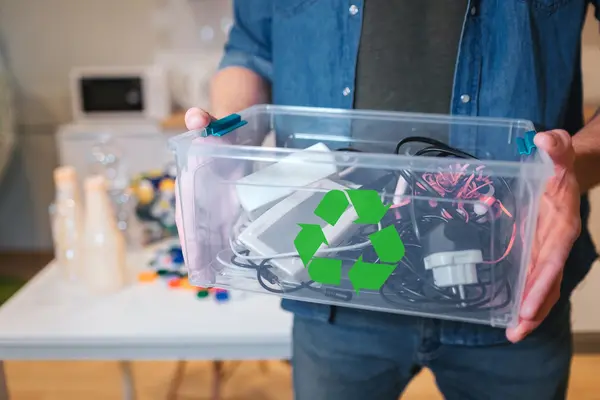 Ein Mann hält eine Plastikkiste in den Händen, die mit Elektro-Schrott gefüllt ist.