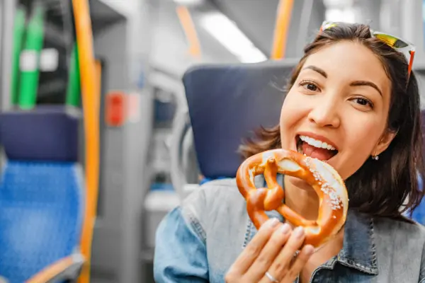 Frau isst eine Bretzel im Zug.