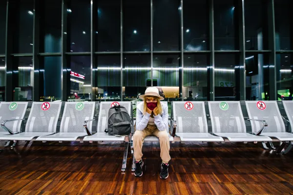 Frau mit Gesichtsmaske sitzt alleine im Flughafen