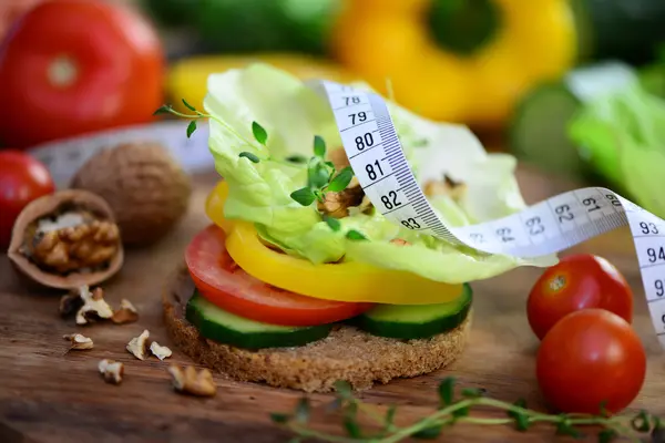 Maßband liegt auf einem Brot, das mit Salat und Gemüse belegt ist
