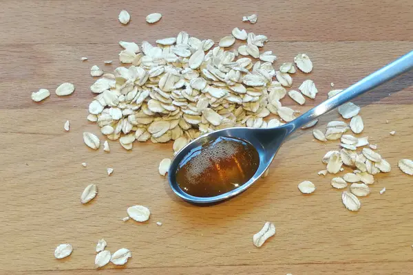 Ein Löffel mit Hafersirup liegt auf einem Holztisch, daneben liegen Haferflocken