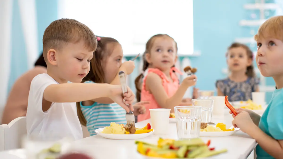 Kinder sitzen in der Kita am Tisch und essen