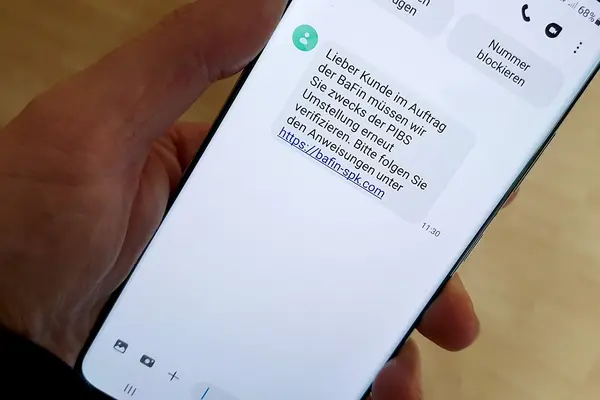 Hand hält Smartphone, Display zeigt betrügerische SMS zum Online-Banking