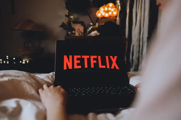 Person sitzt auf Sofa mit Laptop. Auf Bildschirm steht Netflix