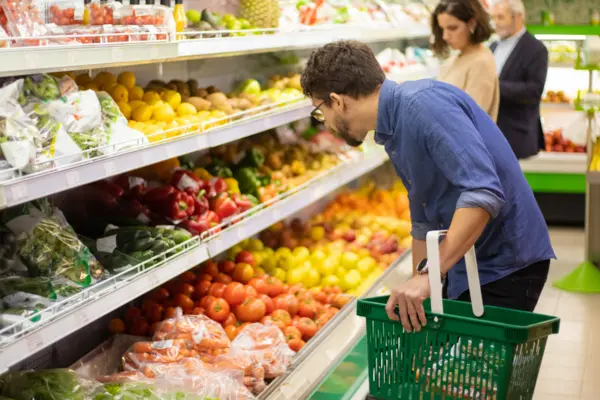 Mann mit Einkaufskorb im Supermarkt vor der Obstauswahl