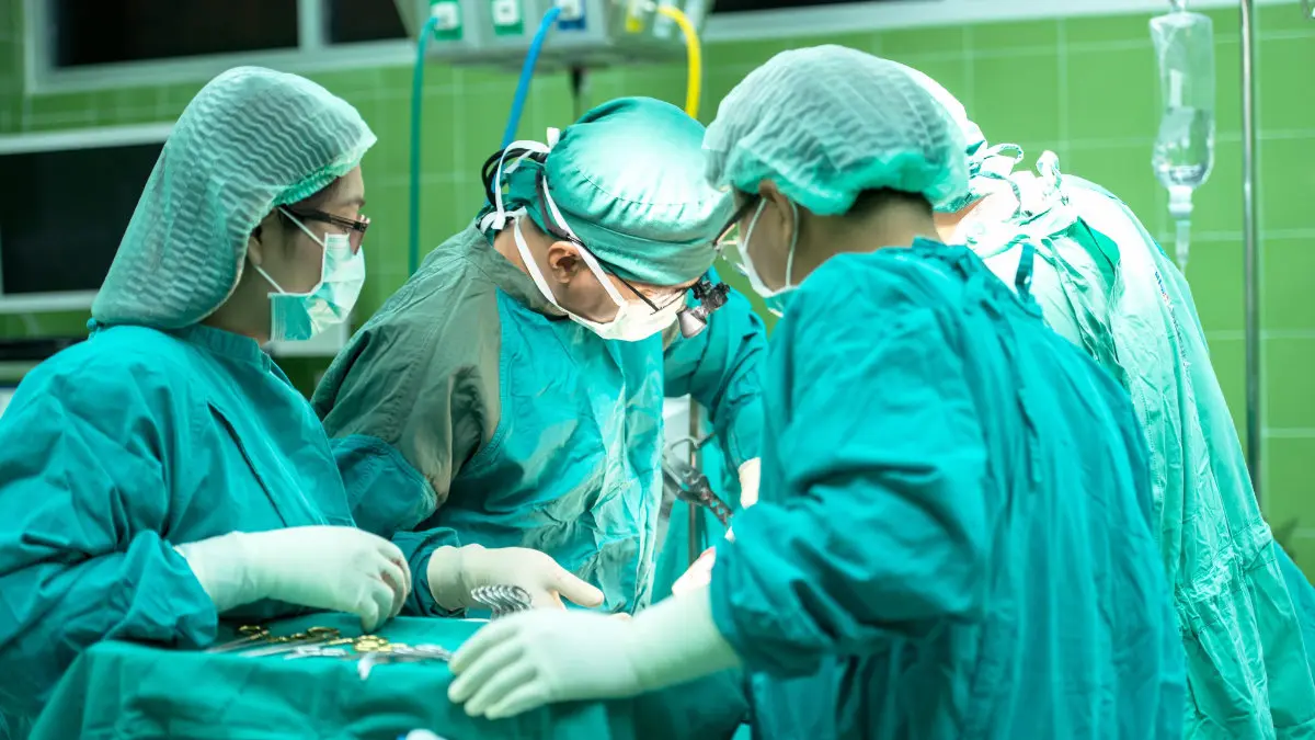 Blick in einen Operationssaal im Krankenhaus mit drei Personen in grüner Schutzkleidung während einer Operation