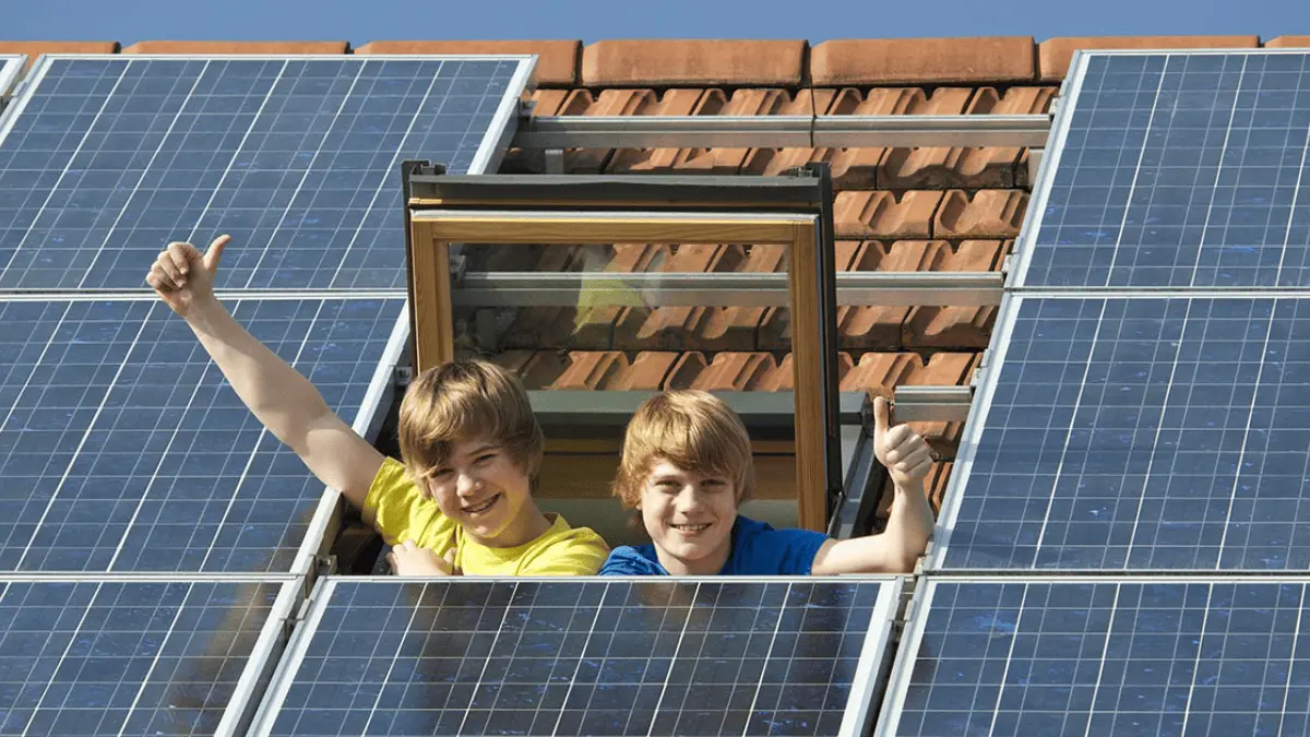 Kinder winken aus dem Dachfenster neben einer Photovoltaikanlage