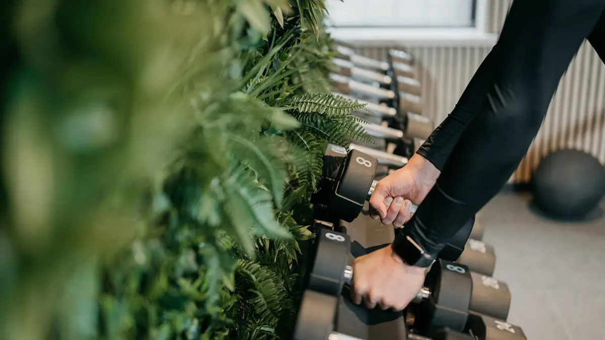 Frau in Fitnesskleidung greift zwei Hanteln aus einer Ablage