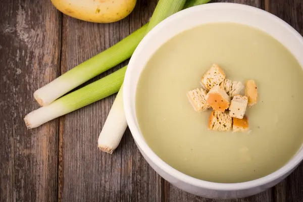 Einige Stangen Lauch und eine Schale mit Kartoffel-Gemüsesuppe