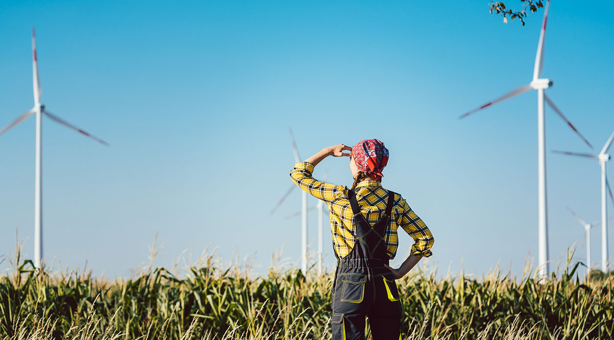 Eine Frau in Arbeitskleidunng steht auf dem Feld und blickt auf Windräder