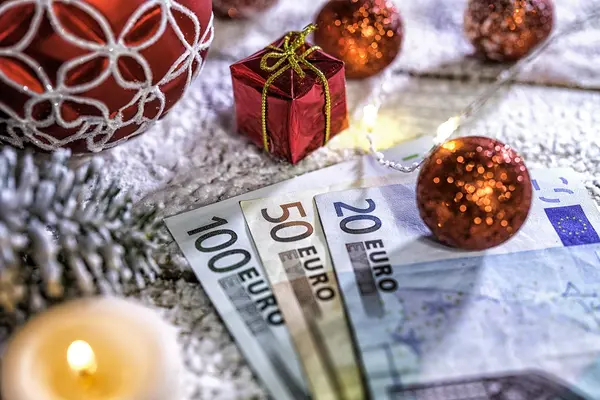 Eine Christbaumkugel liegt auf Euro-Scheinen um Weihnachtsgeld darzustellen