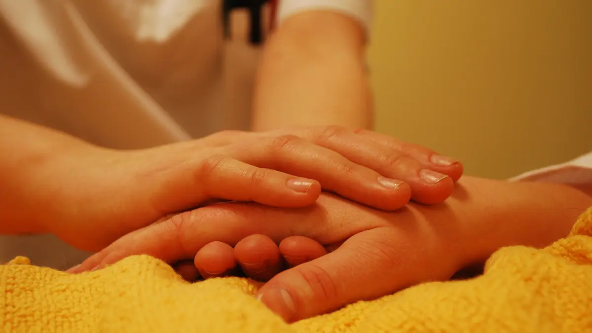 Zwei Hände halten die Hand eines kranken oder alten Menschen