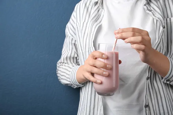 Eine Hand hält ein Glas mit einer hellrosa Trinkmahlzeit, drei Finger der anderen Hand umschließen den Strohhalm, der im Getränk steckt.