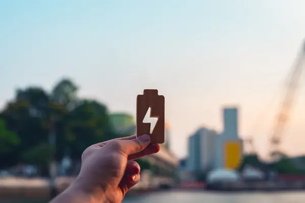 Mensch hält Batteriesymbol vor Stadtkulisse