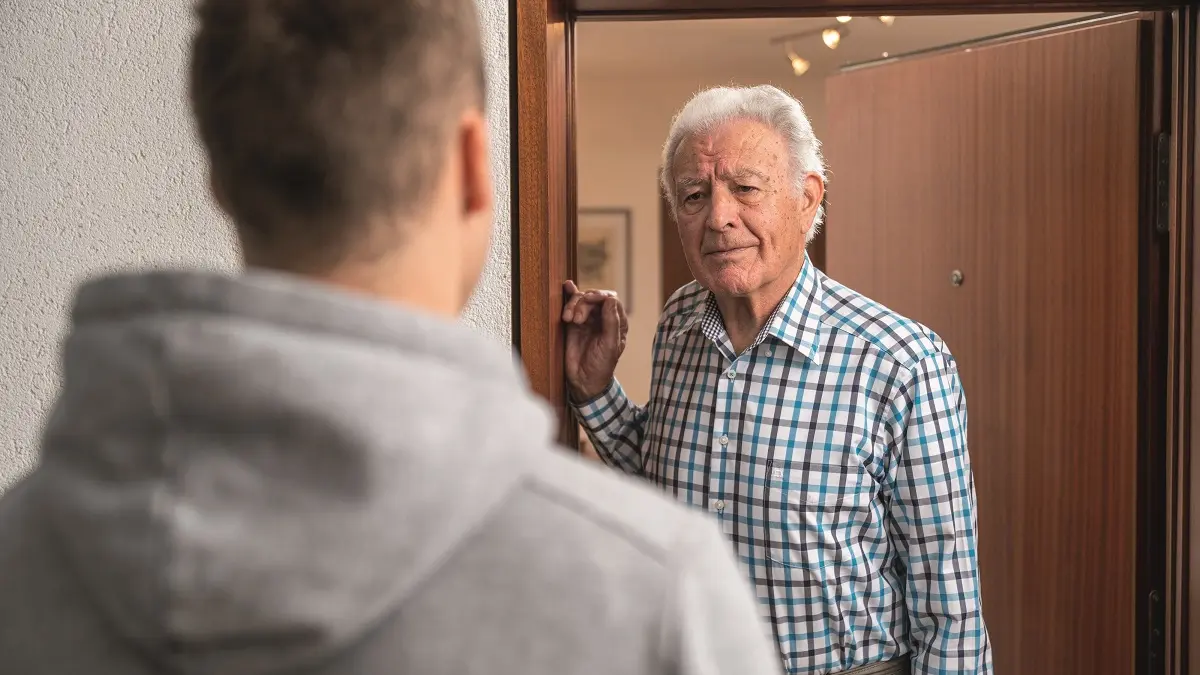 Älterer Mann öffnet seine Wohnungstür. Davor steht ein junger Mann.