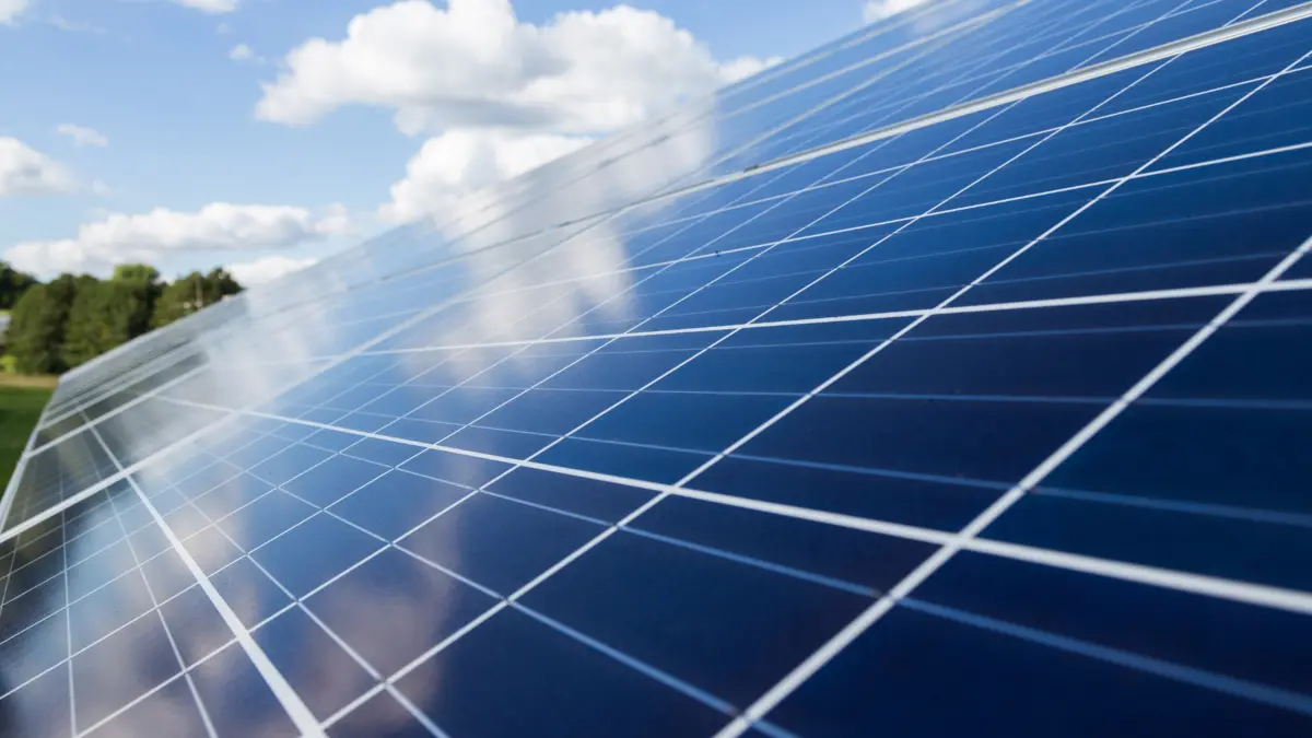 Nahaufnahme Photovoltaikanlage, im Hintergrund sind Bäume und eine Wolke am Himmel zu sehen