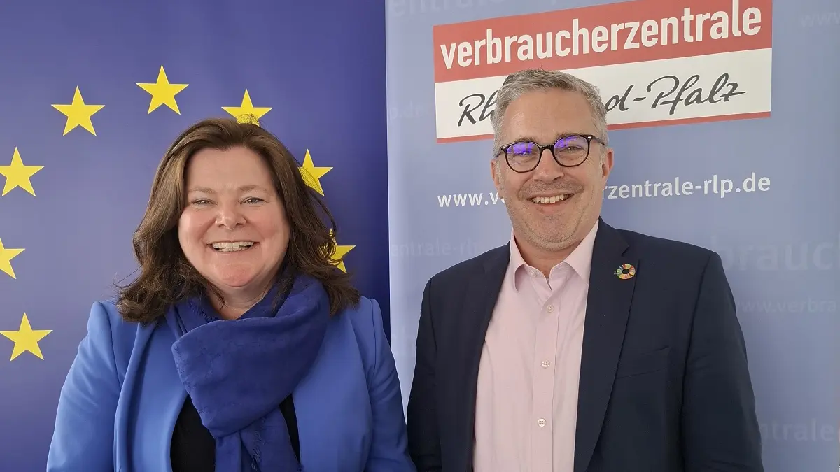 Eine Frau und ein Mann stehen vor einem Roll-up der Verbraucherzentrale und lächeln in die Kamera.