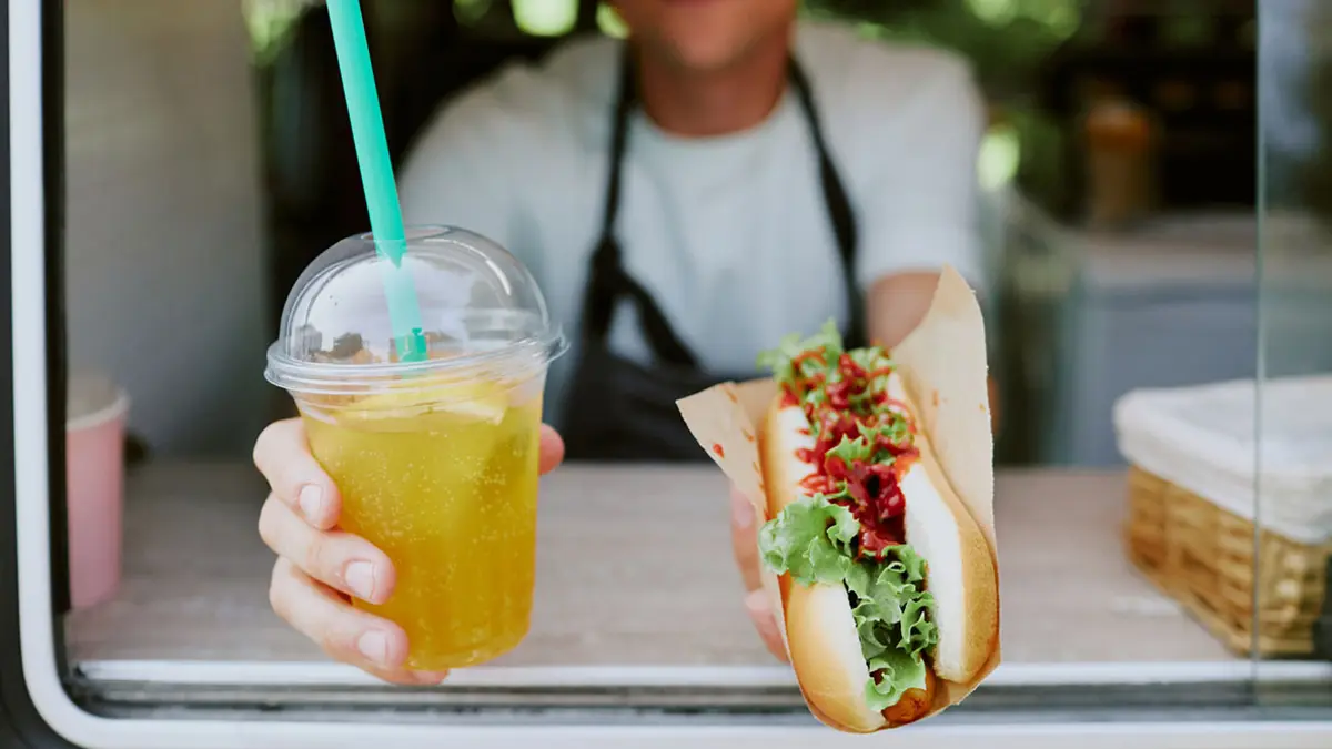 Jemand reicht einen Hotdog und einen Softdrink aus einer Imbisswagen nach draußen