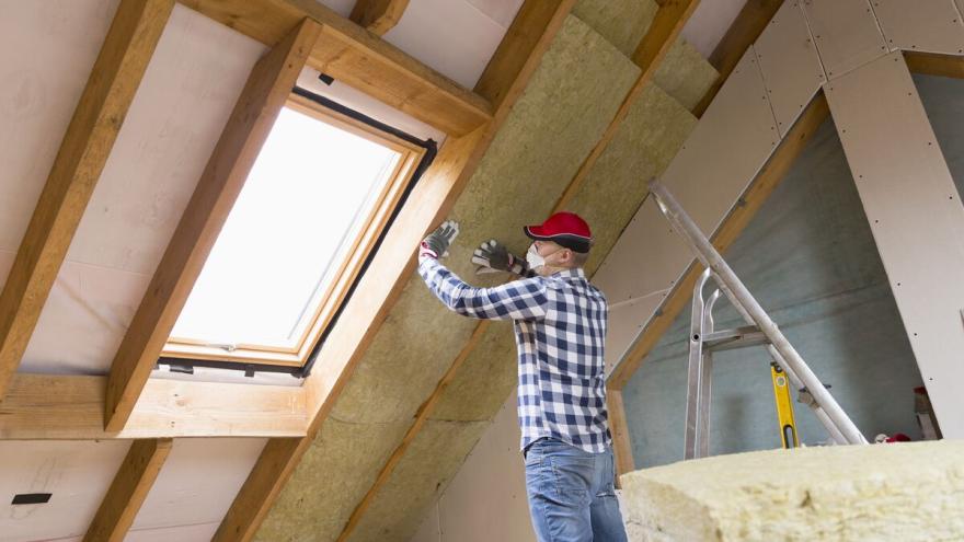 Bauarbeiter dämmt Zwischensparren im Dach neben Dachfenster