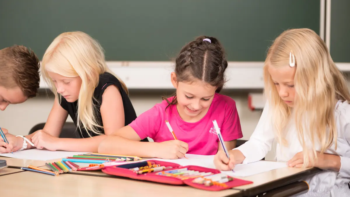 Drei Grundschulkinder sitzen an einem Schultisch und lernen
