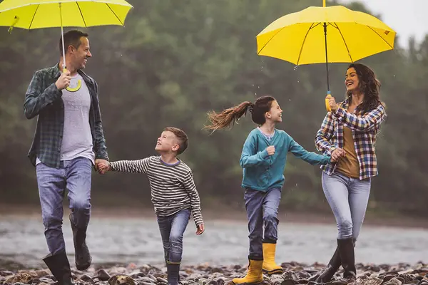 Versicherungen für unterschiedliche Lebenslagen: Erwachsene und Kinder laufen im regen unter Regenschirmen 