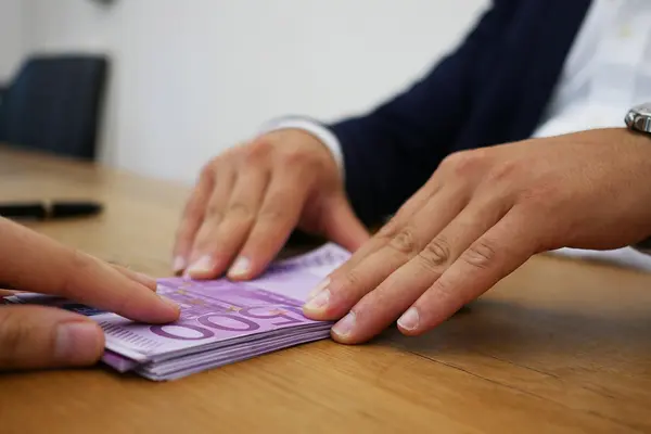 Hände schieben einen Stapel 500-Euro-Schein über einen Tisch