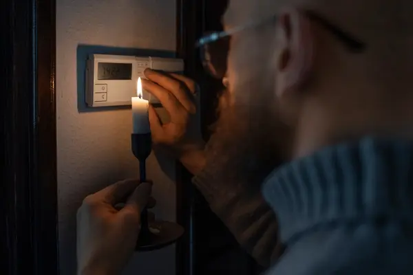 Ein Mann leuchtet bei Stromausfall mit einer Kerze am Sicherungskasten